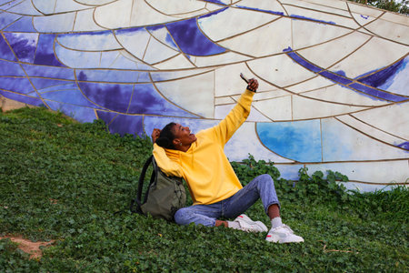young african american man sitting on the grass and taking a selfieの写真素材