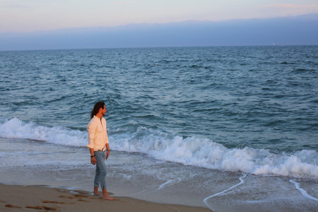 Beautiful young woman standing on the beach with sea in the backgroundの写真素材