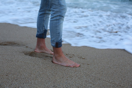 Feet of a man in jeans on the sand by the seaの写真素材