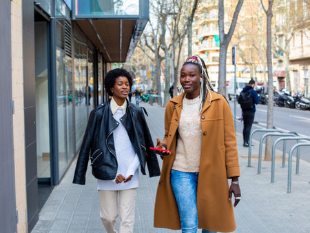 two african american women walking in the city with phone in handの写真素材
