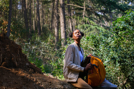 Young african american woman hiker with backpack sitting on ground in forestの写真素材