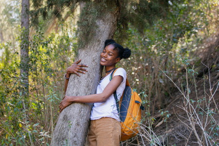 young happy black african american woman with backpack climbing tree in forestの写真素材