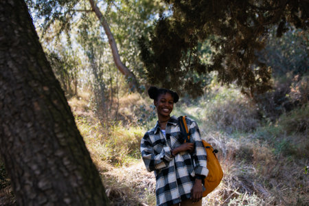 Portrait of happy african american woman with backpack standing in forestの写真素材