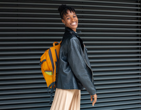 young african american woman in stylish leather jacket and skirt with backpackの写真素材