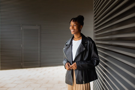 young happy and beautiful black afro American woman in leather jacket and skirt smiling cheerful and confident standing outdoors in urban background looking forwardの写真素材