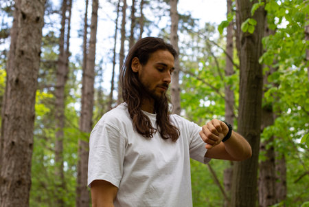 Young man in a white T-shirt in the woods looking at his watch