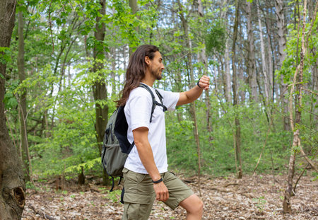 A young man with a backpack is hiking in the woods. A guy with a backpack walks through the woods.の写真素材