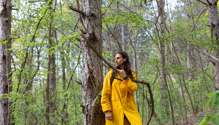 A woman in a yellow raincoat stands in the woods and looks at the camera.の写真素材