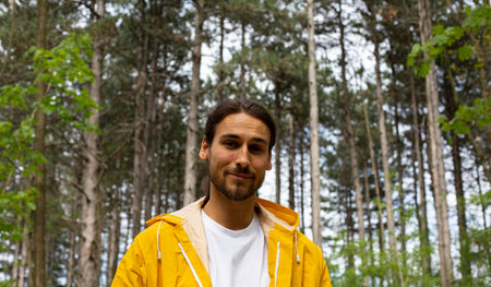 Portrait of young man with beard in yellow raincoat in forest