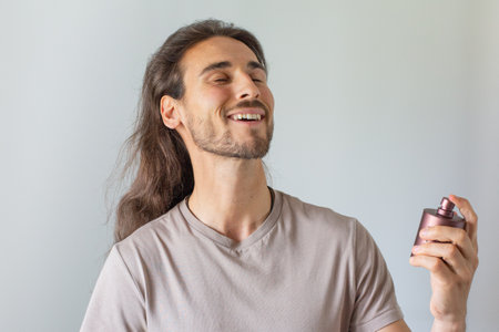 Handsome man with long hair holding bottle of perfume and smiling