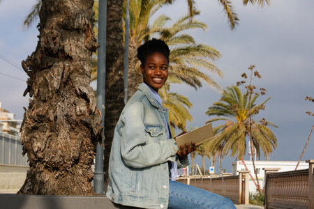 Portrait of a smiling african american woman sitting on a bench and using tablet computerの写真素材