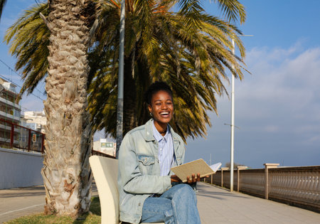 Portrait of young african american woman sitting on bench and reading book