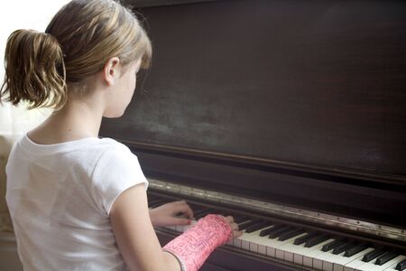 Photo of Maggie in a pink cast playing the piano.の写真素材