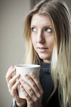 Pretty young blonde woman drinking her morning coffee.の写真素材