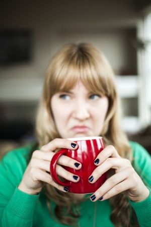 Portrait of a young woman staring straight making an ugly face while holding a cup of coffee.の写真素材