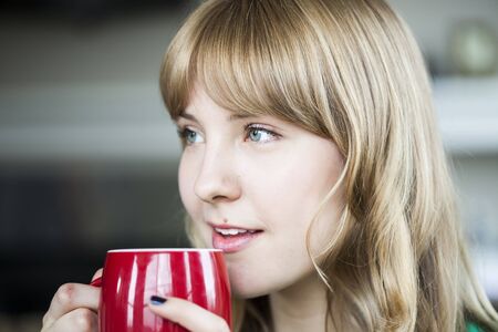 Portrait of a young woman staring straight ahead into the camera holding a cup of coffee.の写真素材