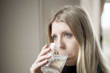 Pretty young blonde woman drinking a glass of water.