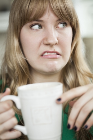 Portrait of a young woman making an ugly face and holding a cup of coffee の写真素材