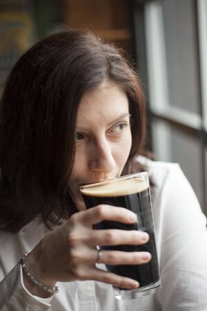 Portrait of a young woman drinking a pint of beer.の写真素材