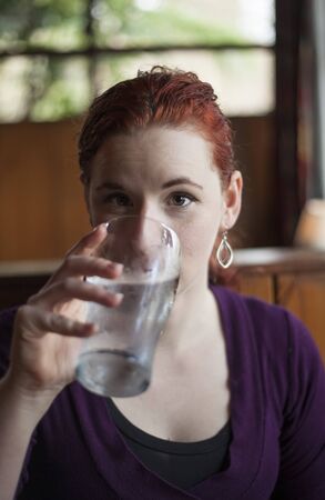 Beautiful young woman with red hair drinking water with ice from a pint glass.