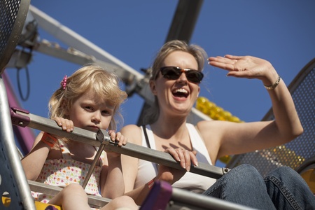 Beautiful, blonde-haired mother and daughter on a ride at the fair.の写真素材