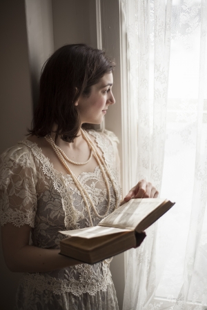 Portrait of a young woman in a vintage white wedding dress reading a book の写真素材