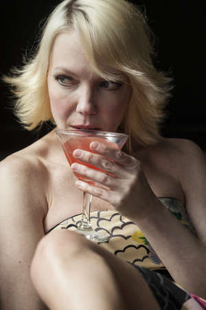 Portrait of a blonde woman drinking a pink martini.