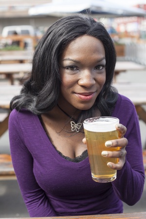 Young African American woman drinks a pale ale from a pint glass.の写真素材
