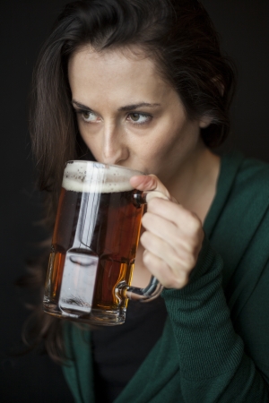 Beautiful young woman with brown hair and eyes holding a mug of beer の写真素材