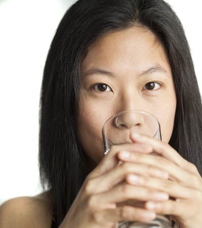 Beautiful Asian woman with brown hair and eyes drinking water from a glass.の写真素材