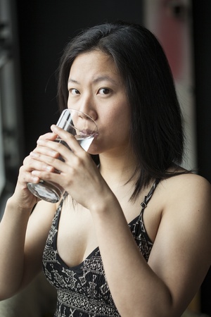 Beautiful Asian woman with brown hair and eyes drinking water from a glass.の写真素材
