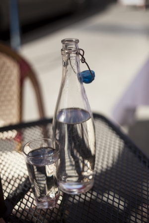 Carafe and glass filled with water sitting on a metal cafe table on a sunny day.の写真素材