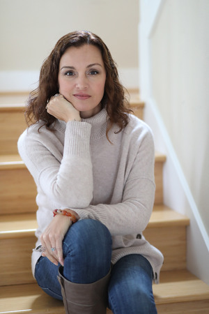 Photo of a very attractive 40-year-old woman with brown hair and eyes. She is sitting on her stairs.の写真素材
