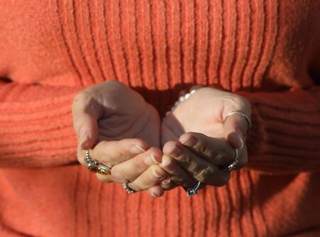 Photo of a woman in an orange sweater. She has her hands cupped in front of her.の写真素材