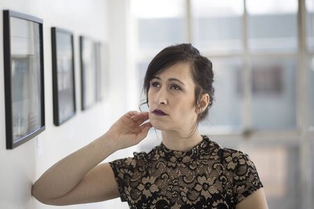 Photo of a very attractive adult woman with brown hair and eyes. She is in a stylish black dress and standing in an art gallery. の写真素材