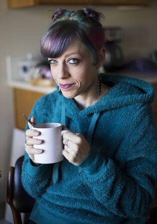 Photo of a very attractive woman with beautiful blue eyes and colorful hair. She is looking straight at the camera and enjoying a morning cup of coffee.の写真素材