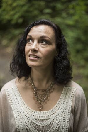 Photo of a very attractive 40-year-old woman with brown hair and eyes. She is standing in a wooded are and wearing a white top.の写真素材