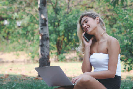 Beautiful woman using smart phone under the tree, Concept of freelance working background.の写真素材