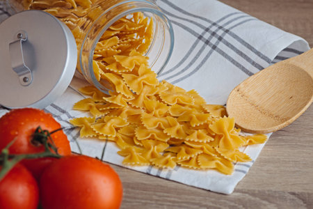 Pasta on a tea towel flows out of a jar with three tomatoes in the foreground
