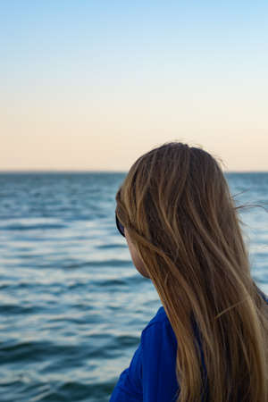 young blonde girl looking sea and blue skies back viewの写真素材