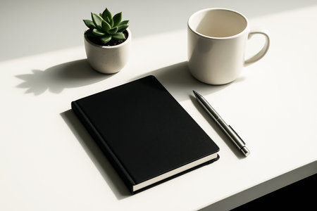 Black notebook, pen and cup of coffee on white table. Minimal style.の素材