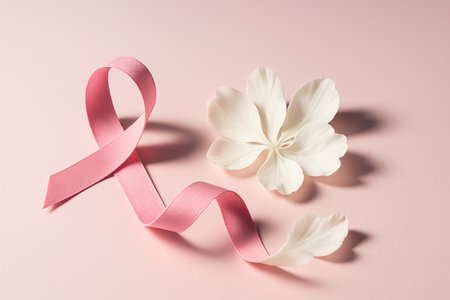 Breast cancer awareness pink ribbon and white flower on pink background.の素材