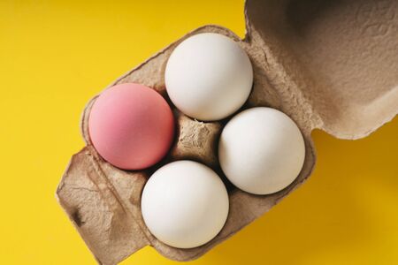 Top view - One pink egg and three white egg in a box over yellow background.の写真素材