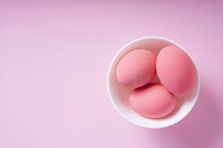 Top view - Three pink eggs inside the white bowl over pink background.の写真素材
