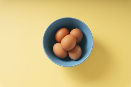 Top view - Organic chicken brown egg inside bowl over yellow background.