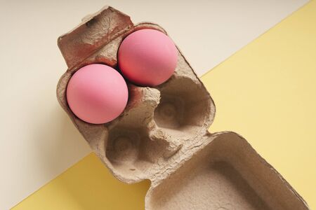 Top view - Two pink eggs in a box over beige and yellow background.