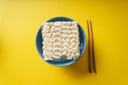Top view - Instant noodle in a bowl and chopstick over yellow background.の写真素材