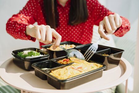 Beautiful asian thai long dark hair woman in red shirt taking using fork and spoon eating food lunch...
