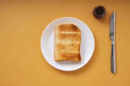 Top view - Grill home made organic sliced bread on white plate and jam in a jar with knife.の写真素材