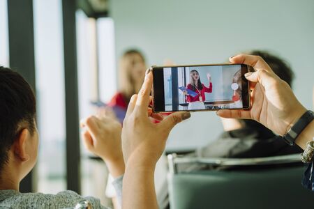 Beautiful young asian thai businesswoman in red shirt giving present in front of the room. People taking picture or record the video of the presentation with smartphone.の写真素材